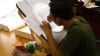 An animation student wearing a green shirt, focused on tracing his human figure drawings via a lightened drawing table.