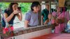 A woman taking photo of the traditional weaving loom while a woman with glasses inspects the loom; with two other women looking over and guiding